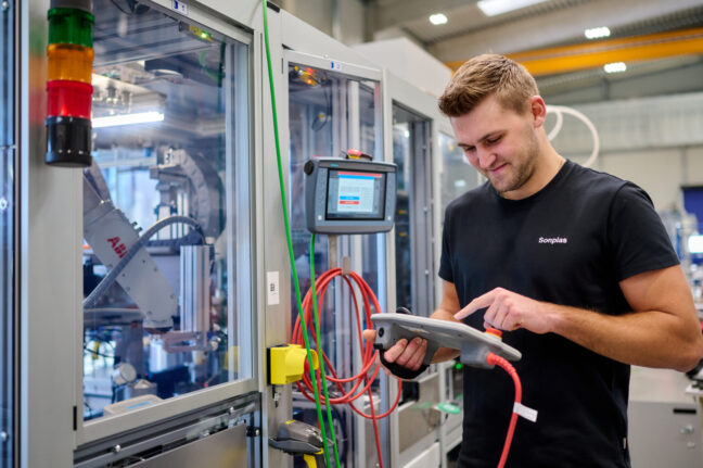 Sonplas Mitarbeiter steht neben einer Anlage und schaut dabei auf das HMI